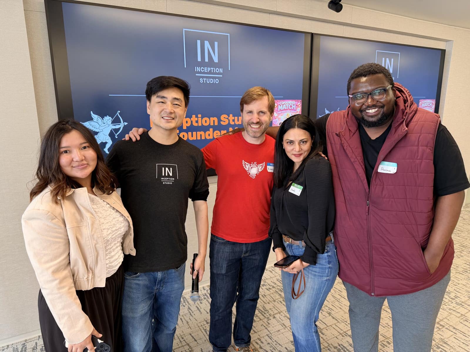 Dominic and four others at a cofounder matching event, name tags on, in front of the event screen.