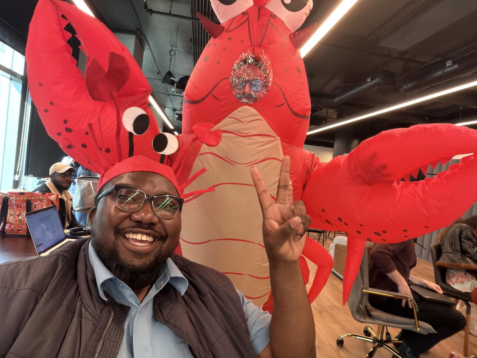 Dominic in a lobster hat next to someone in a full inflatable lobster costume at a coworking space.
