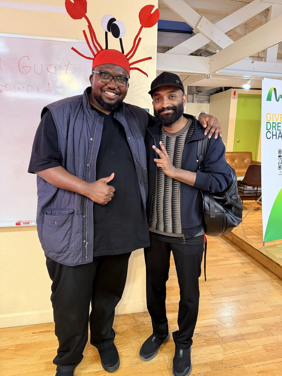 Dominic in a lobster hat with an attendee at a community event, both giving the camera a thumbs up.